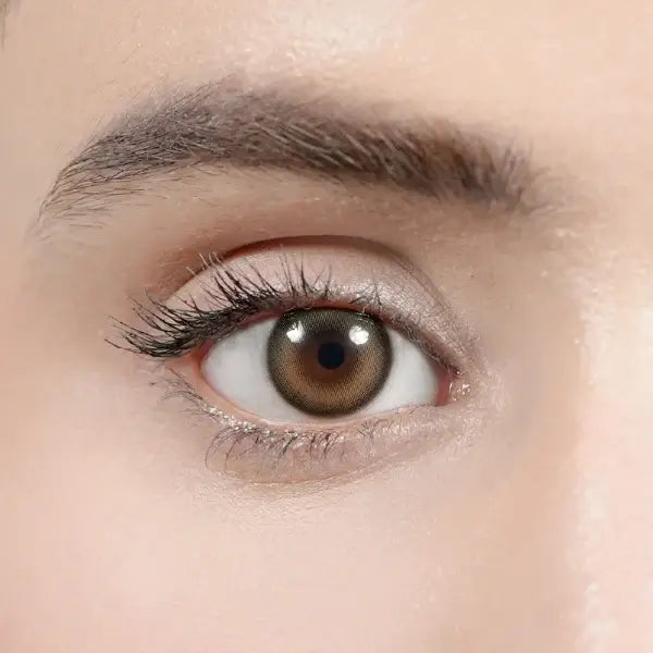 Extreme close-up of a human eye wearing a brown colored contact lens, showing detailed eyelashes, eyebrow, and skin texture.